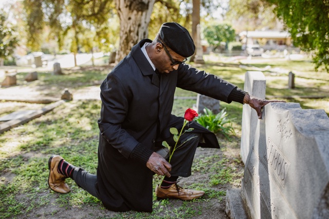 Man holding a rose beside a gravestone