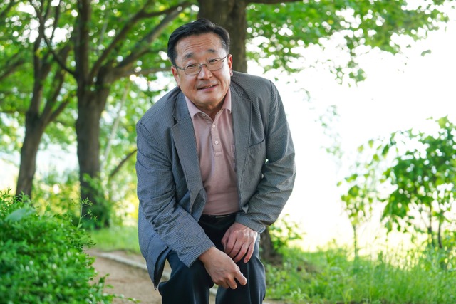 Older man in a suit outdoors beneath trees