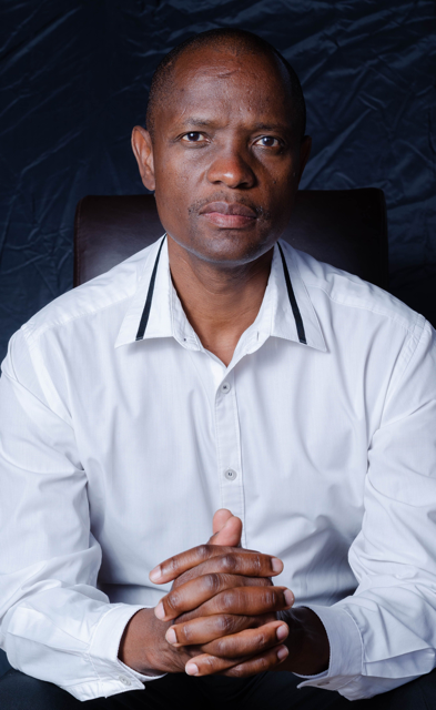 Man in a white shirt seated with his hands clasped